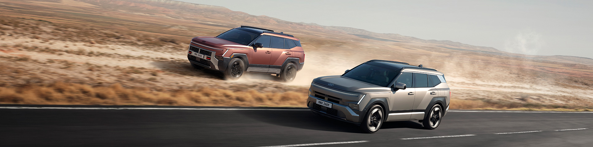 Two all-new Hyundai TUCSON models driving side by side, one on an open road and the other across dusty off-road terrain.