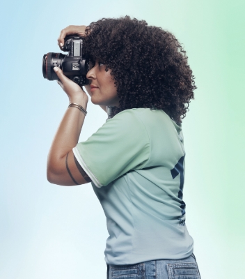 A side view of Nicky Woo taking a photo with her camera. She is wearing a light green Team Century t-shirt.